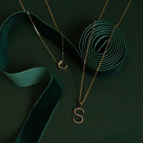 A 9ct yellow gold pendant in the shape of the letter C and a 9ct yellow gold pendant with diamonds in the shape of the lettter S are laying on a green background